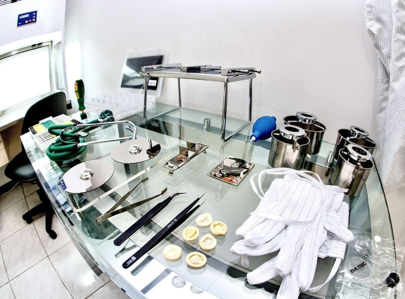 Bancada de laboratório com várias ferramentas de recuperação de dados e sistema de fluxo laminar ativo ao fundo.